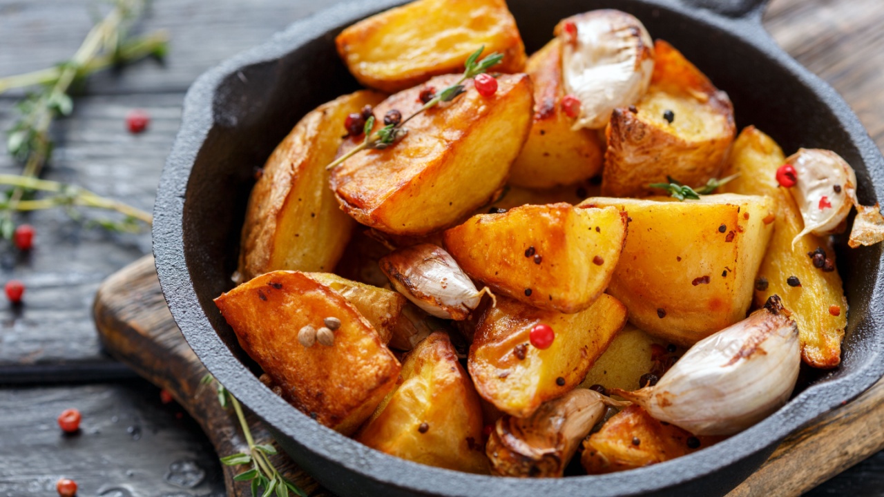 Cast iron skillet with baked potato slices, garlic, pepper and thyme on an old wooden table, selective focus.