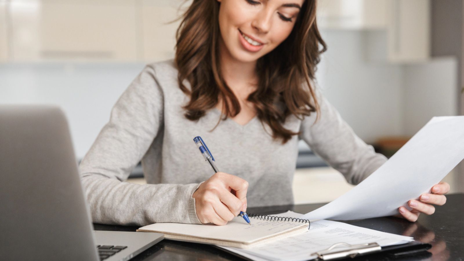 Attractive young woman working on laptop computer while taking notes