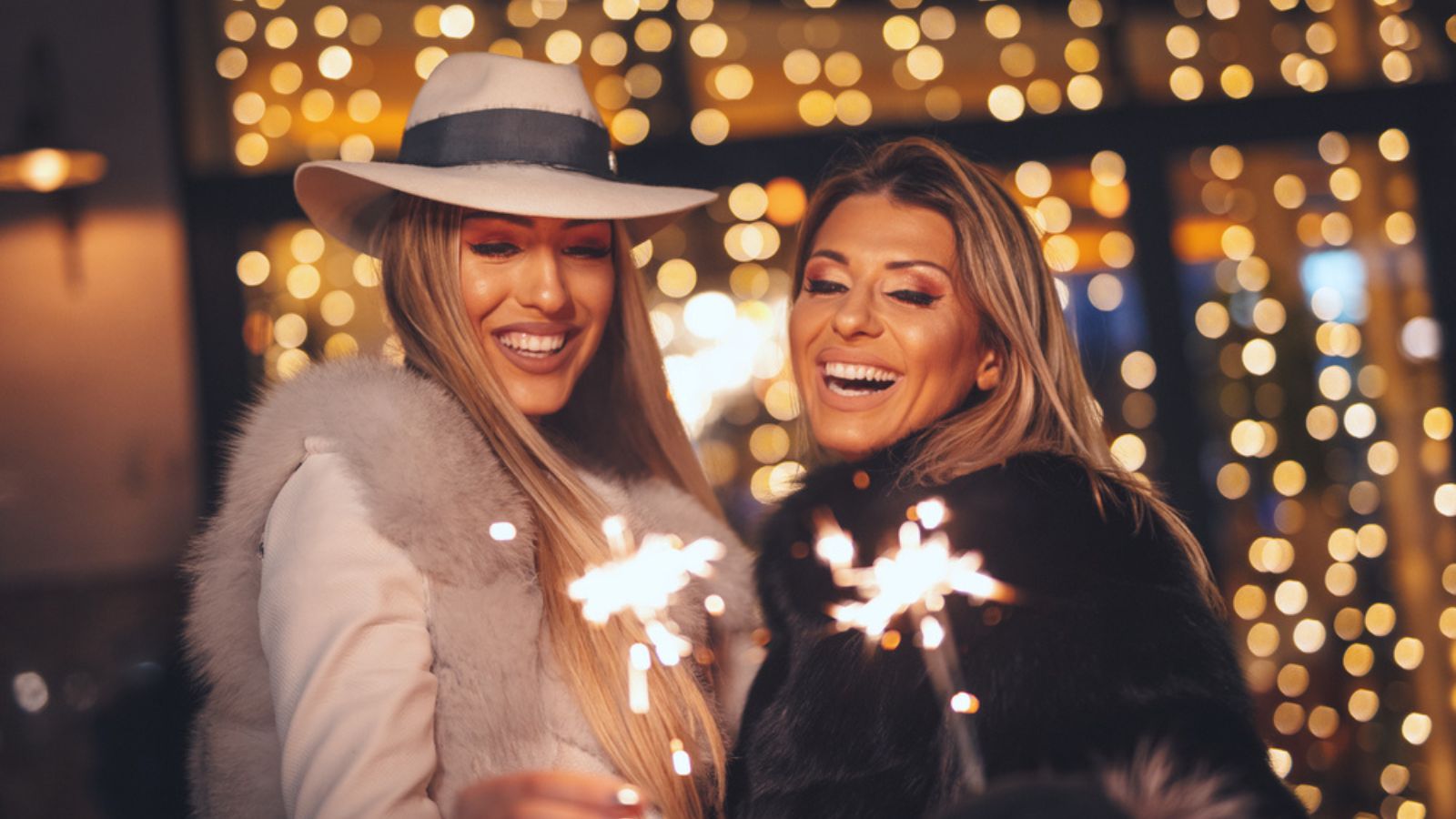 Cheerful young sisters are holding sparklers and having fun at holiday winter night in the city street