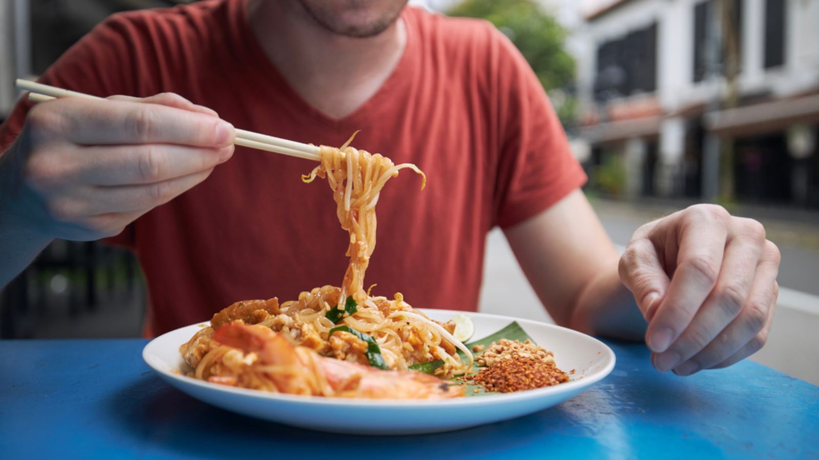 Close-up of chopsticks with Pad Thai food. Man eating in street reastaurant on side of road in Singapore