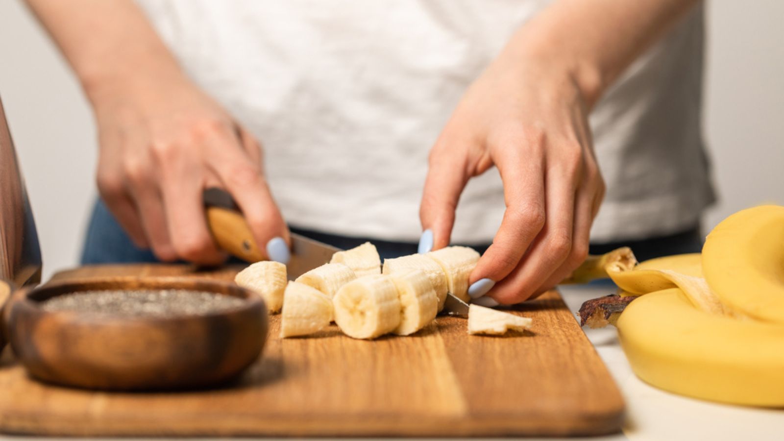 Cropped view of woman cutting organic and sweet bananas on cutting board on white