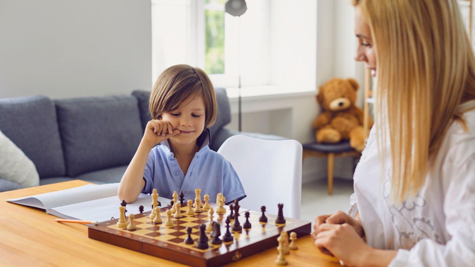Family hobbies. Young mother playing chess with son at home. Little boy engaged in board game with his parent in room