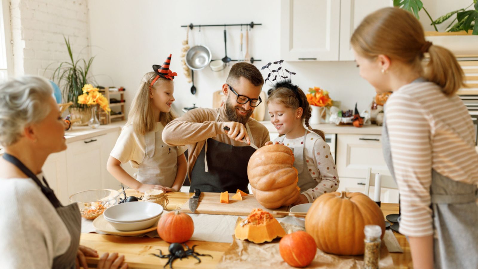 Happy multi generational family smiling and carving jack o lantern from pumpkin while gathering around table during Halloween celebration