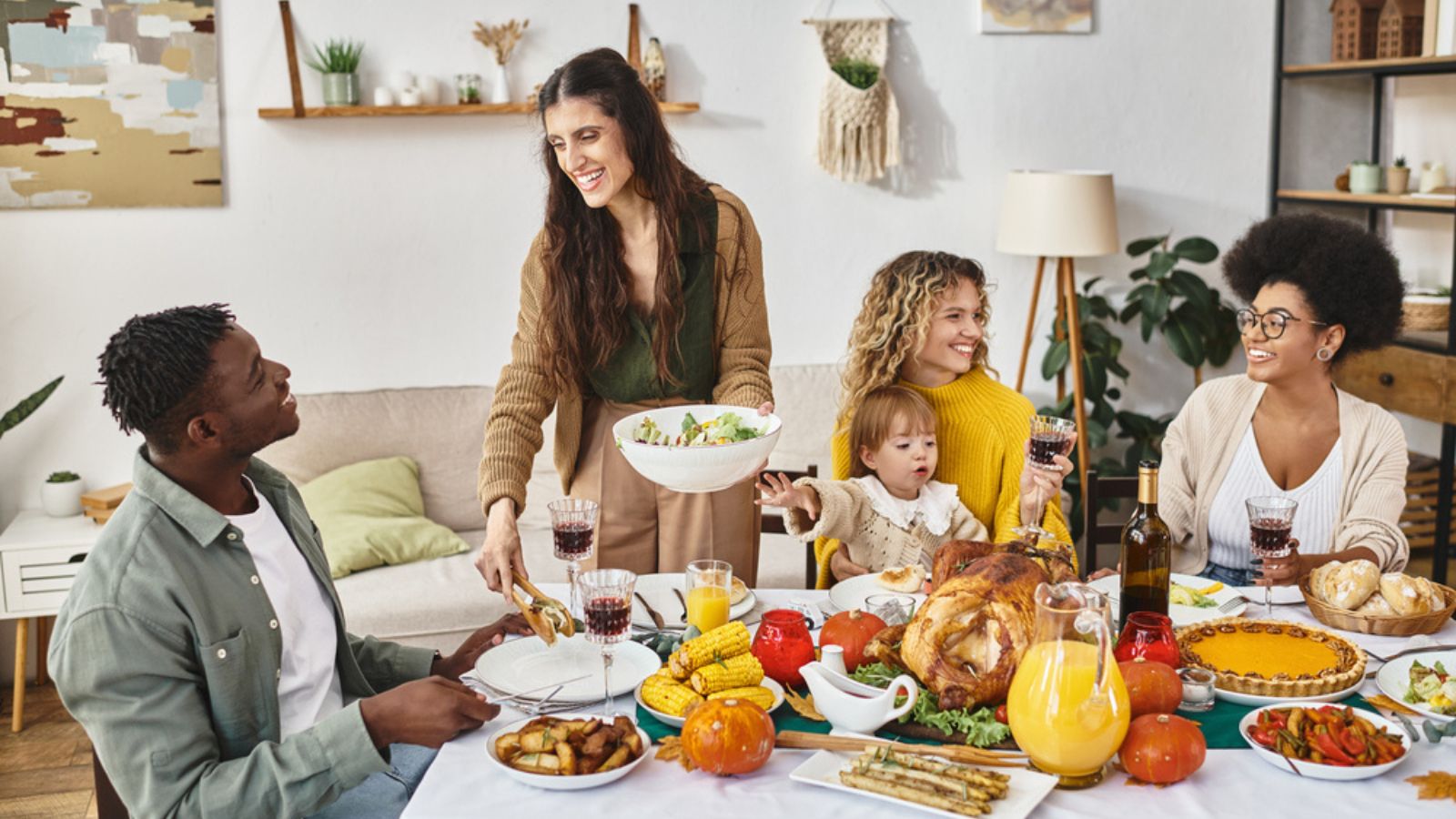 Happy woman serving salad to african american man near friends and family on Thanksgiving day