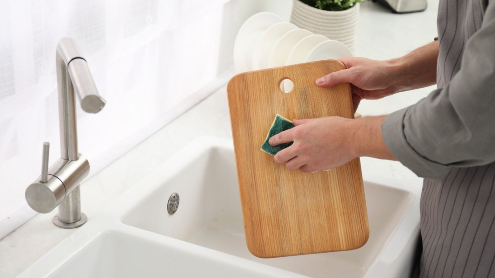 Man washing wooden cutting board at sink in kitchen, closeup