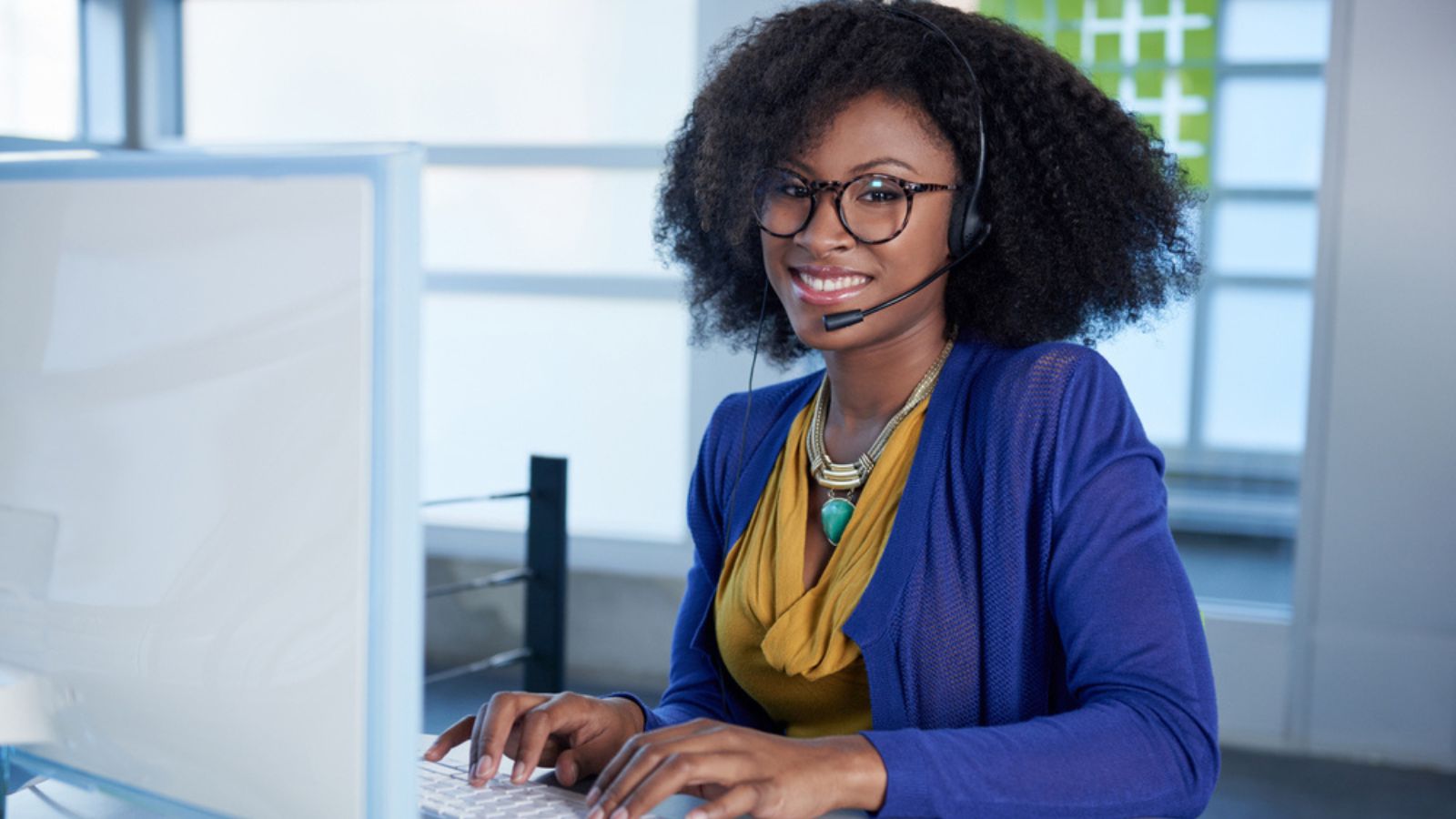 Portrait of a smiling customer service representative with an afro at the computer using headset