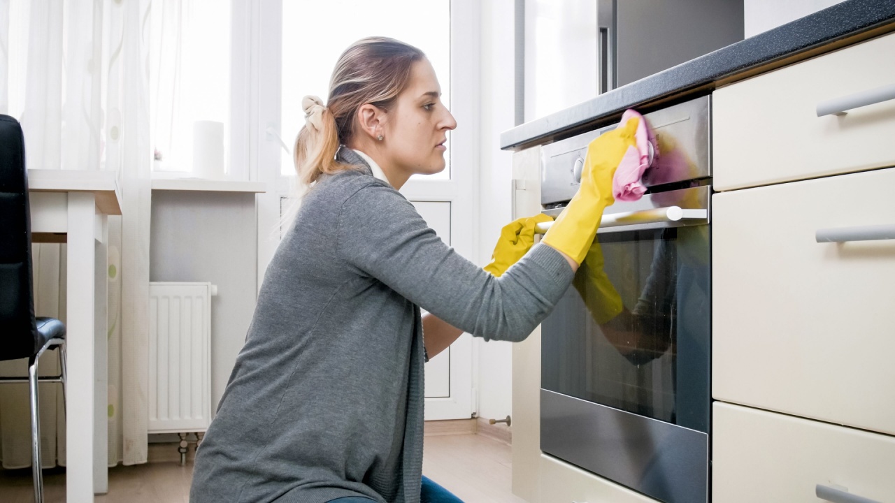 Tired housewife in latex gloves cleaning oven on kitchen