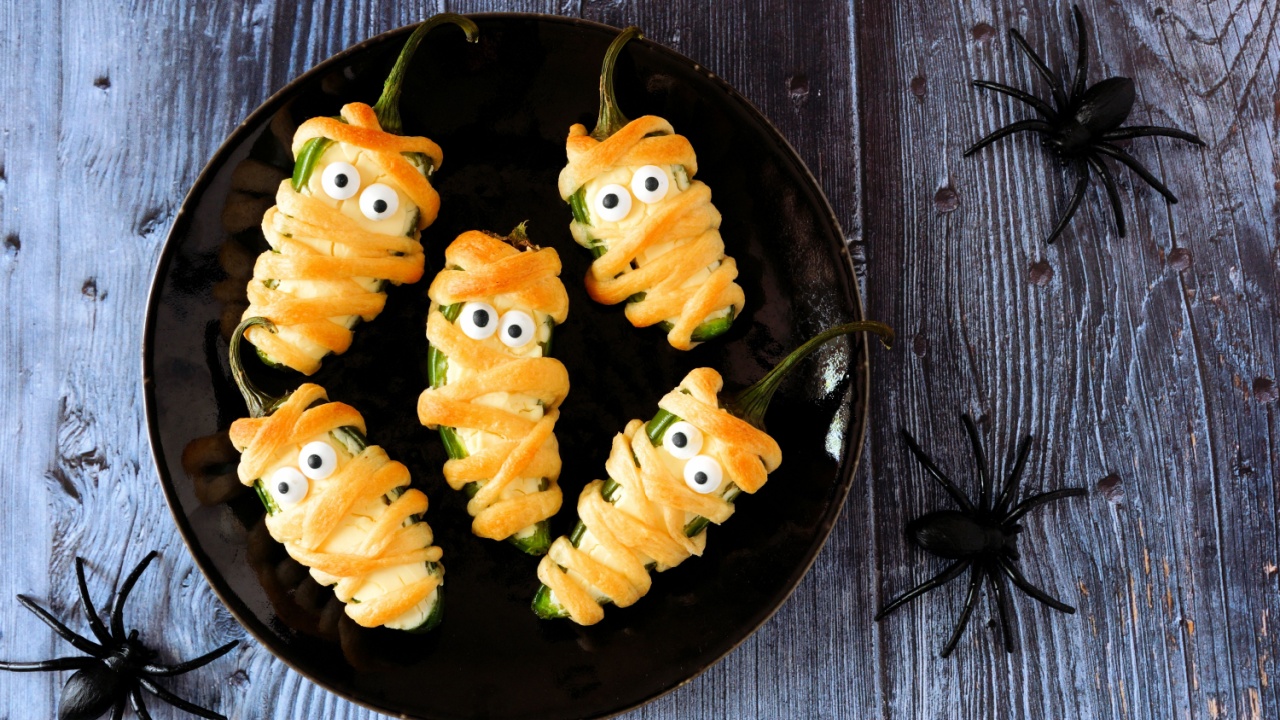 Plate of Halloween mummy jalapeno poppers, top view on with a dark wood background with spiders