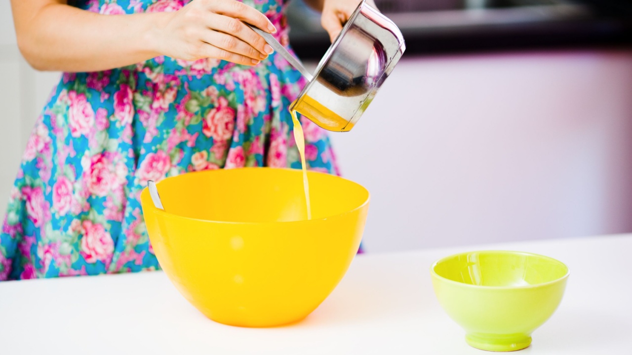Pouring out melted butter from a metallic pot to an orange plastic bowl at homely kitchen