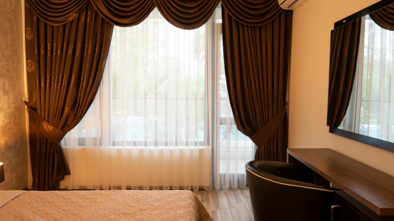 Classy bedroom interior design. Large bed. Room with brown color tone furniture. Windows with long curtains, drapery and sheers. Interior photography