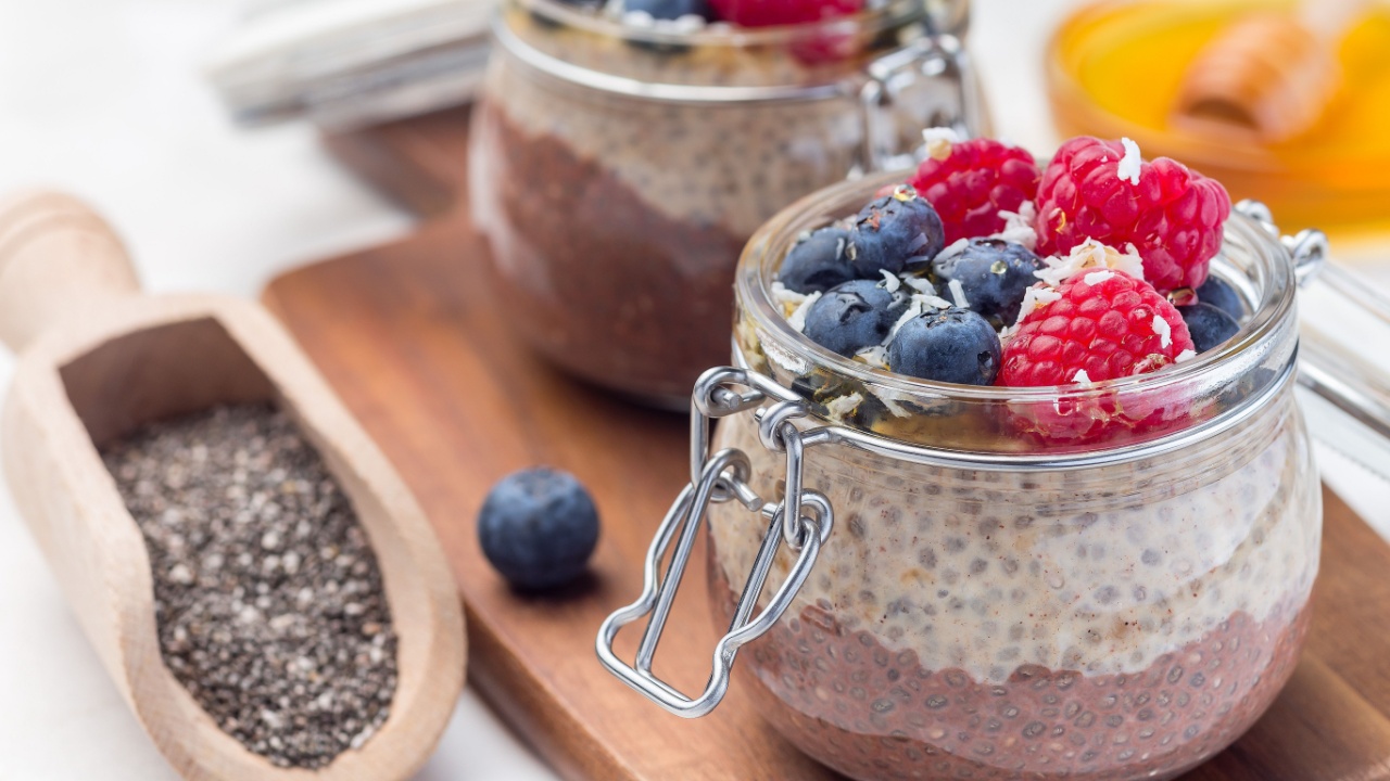 Layered chocolate and peanut butter chia seed pudding in a jar, garnished with raspberry, blueberry, honey and coconut flakes, horizontal