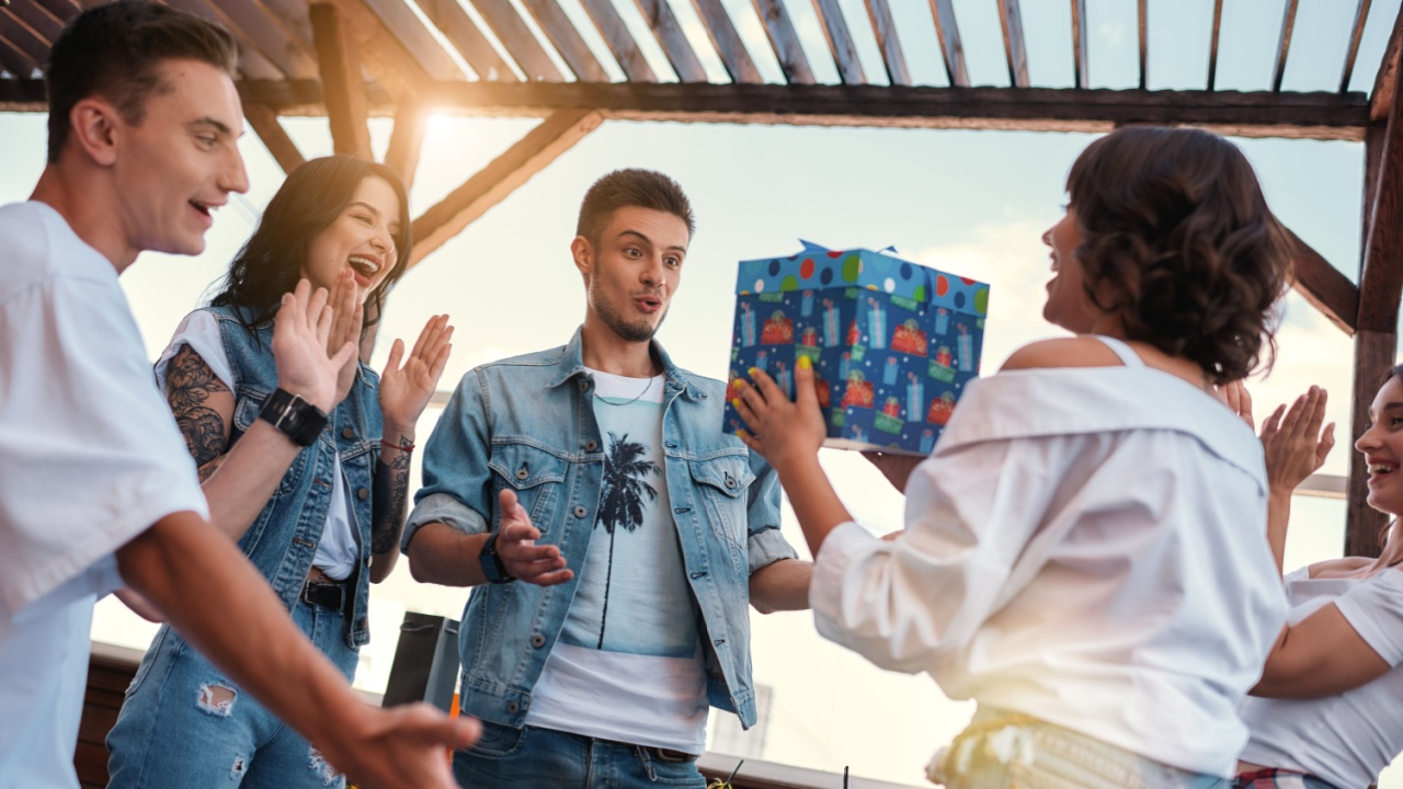 Surprise Young woman is holding a gift box for her friend while standing on the roof around friends