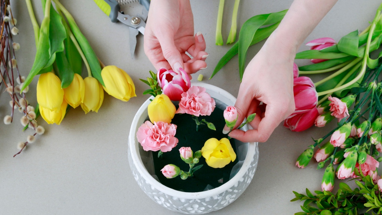 Florist at work: woman shows how to make beautiful floral arrangement with tulip and carnation flowers. Easter home decoration. Step by step, tutorial.