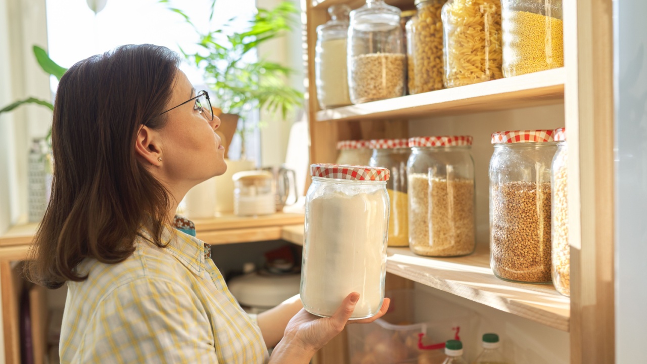 Food storage, wooden shelf in pantry with grain products in storage jars. Woman taking food for cooking