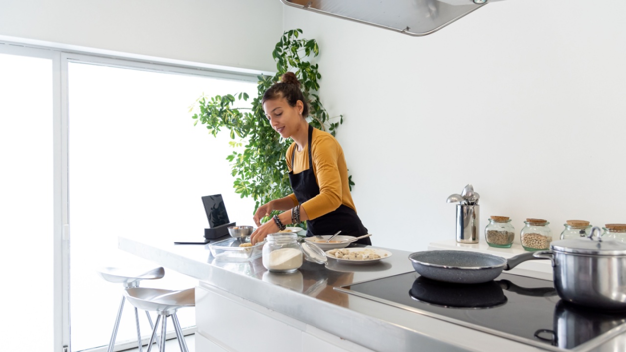 Brunette woman cooking a recipe from a digital tablet in a modern kitchen