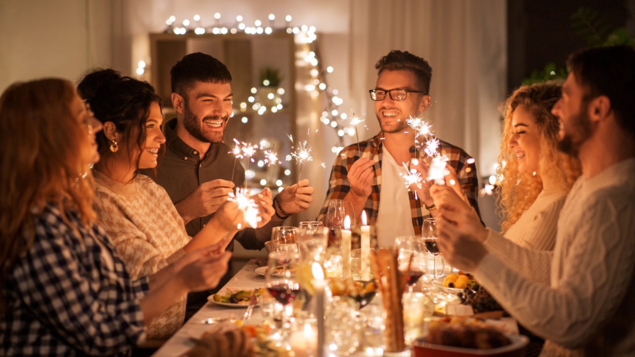 holidays, celebration and people concept - happy friends with sparklers having christmas dinner at home