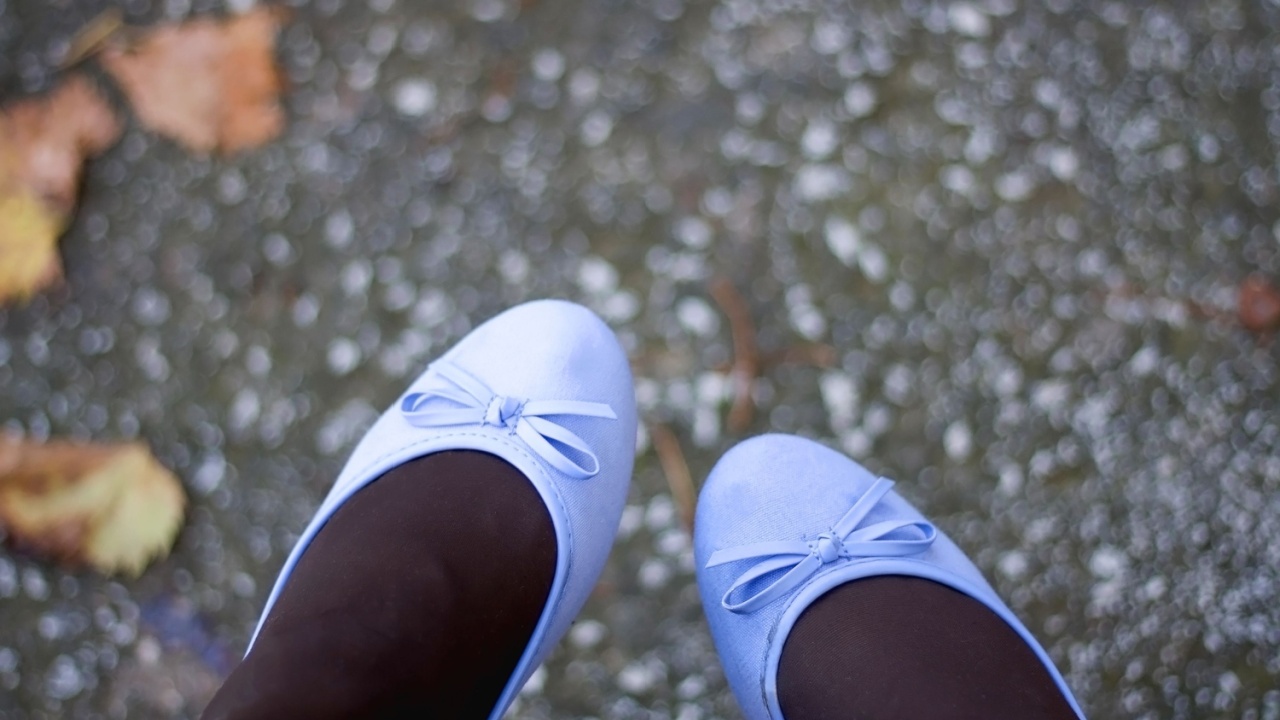 Unrecognizable person in light blue flats and fallen autumn leaves. Selective focus, top view. 