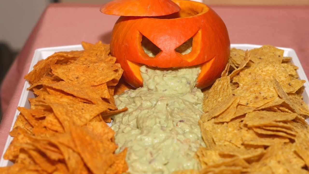 Carved pumpokin filled with guacamole and tortilla chips. Halloween party food. Selective focus.