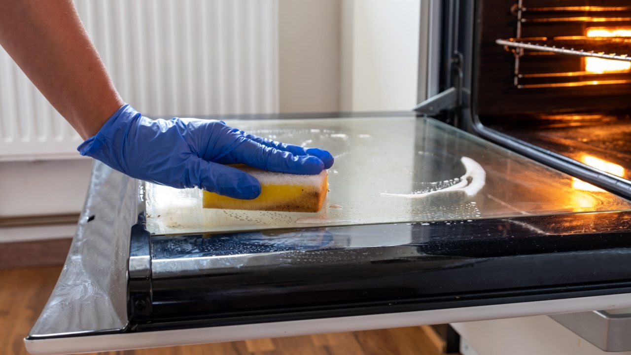 Close up of female hand with blue protective gloes cleaning oven.Woman hand cleaning dirty oven door in the kitcken.