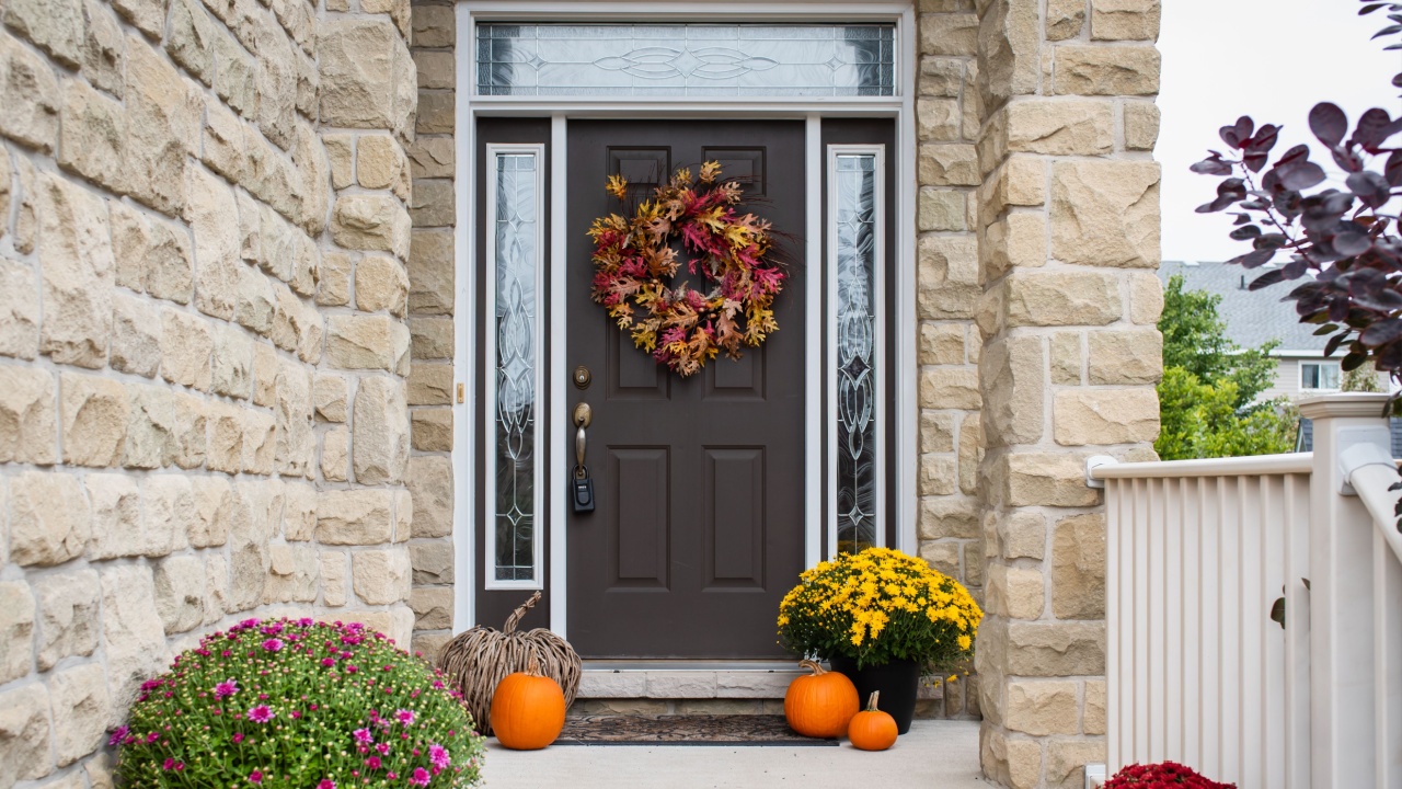 Front door of home decorated for fall with flowers and pumpkins.