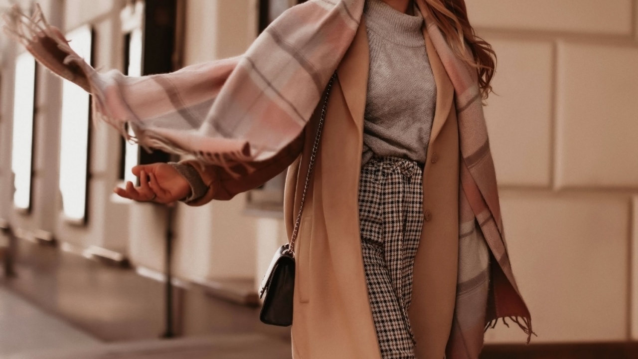 Young woman with cropped head in the grey knitted cozy sweater and brown coat walking on the street. Outdoor portrait in daylight. Warm winter clothes concept