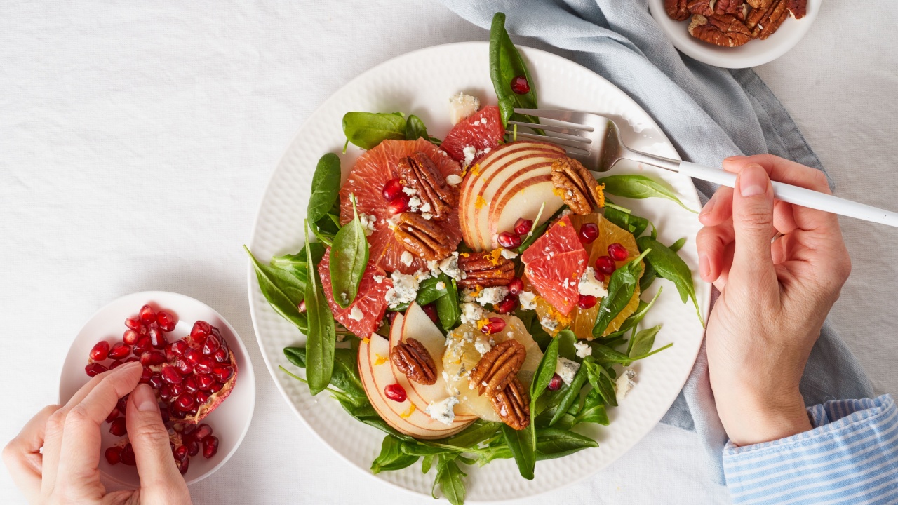 Eating fruits citrus salad with nuts, green lettuce. Balanced food. Top view of woman hands with plate of meal of Spinach with orange, grapefruit, apples, pecans