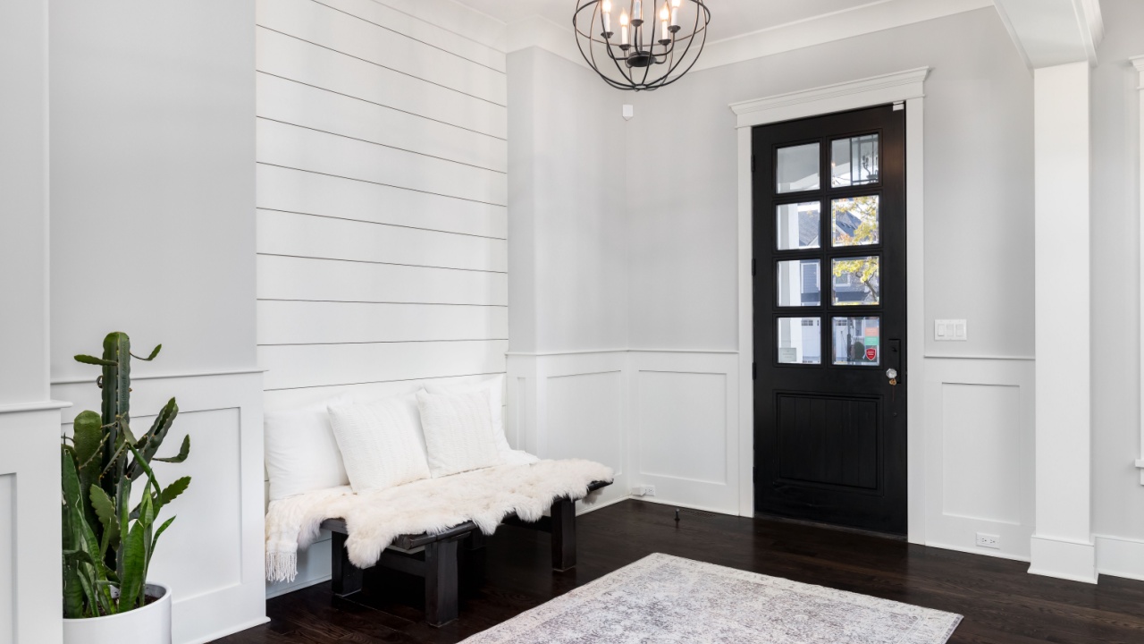 ELMHURST, IL, USA - NOVEMBER 1, 2020: A beautiful foyer entrance with a light hanging above the dark hardwood floors, a bench in front of a shiplap wall, and a dark door with windows.