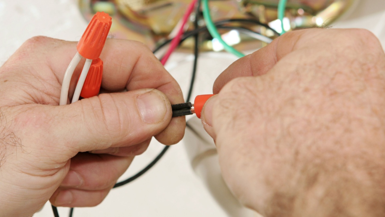 A closeup of an electrician's hands as he connects wires using a wire-nut. All work is being performed to code by a licensed master electrician.