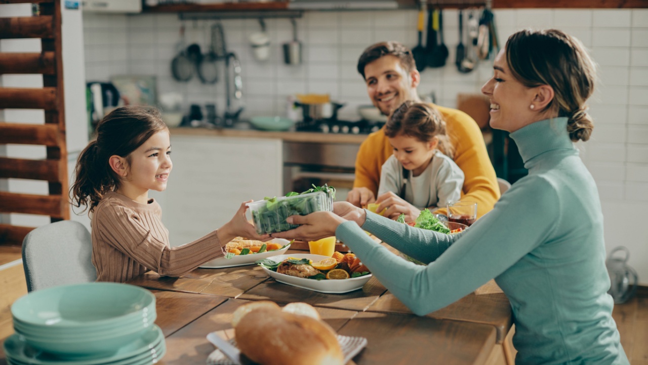 Happy mother passing salad to her daughter during family lunch in dining room. 