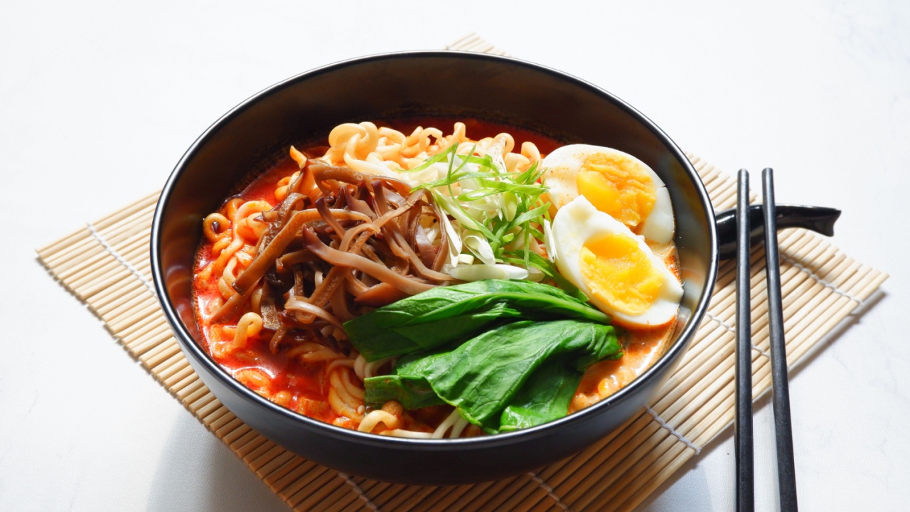 selective focus of spicy ramen served with vegetables topping and boiled egg in a black bowl against white background