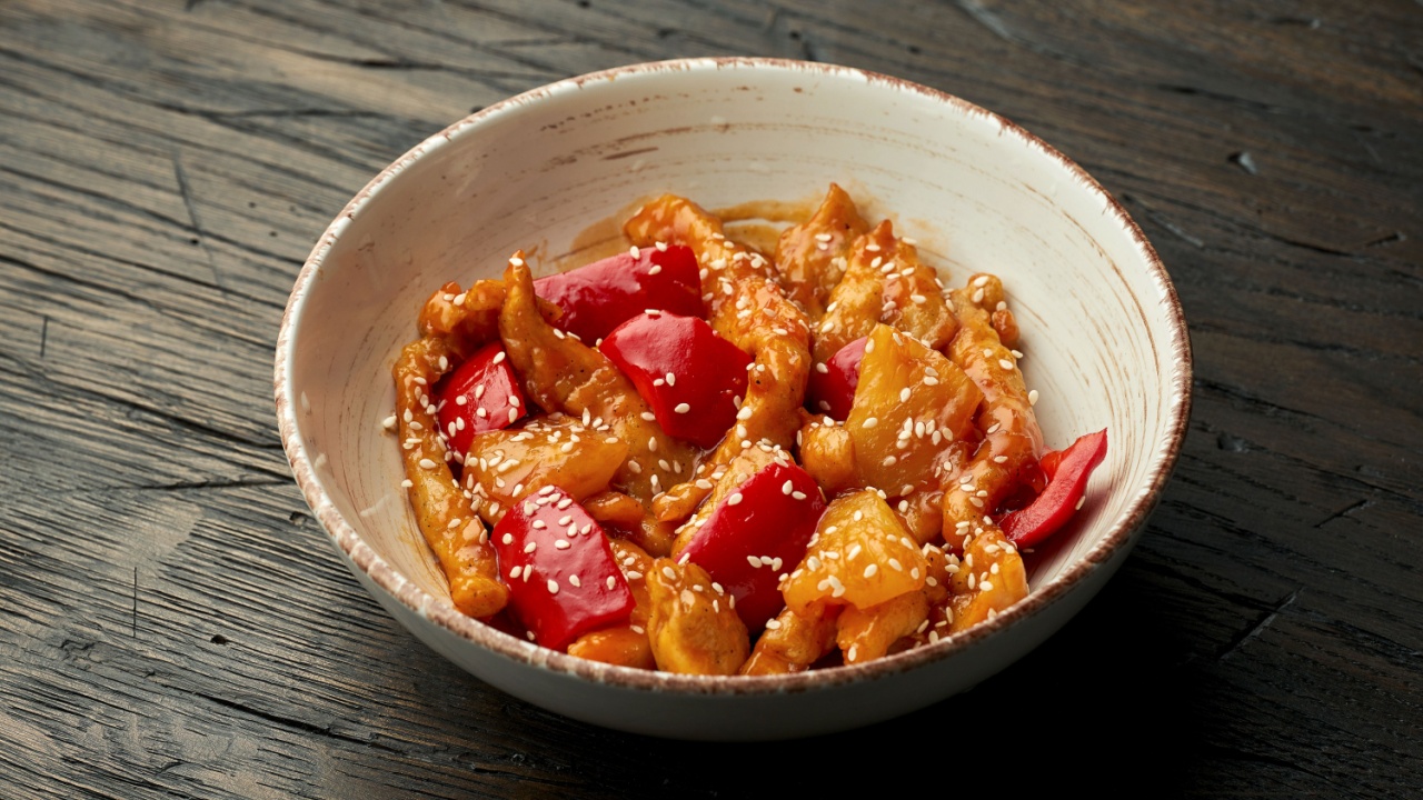Delicious Asian street food - sweet and sour chicken with sesame seeds and bell pepper in a white bowl on a wooden background.
