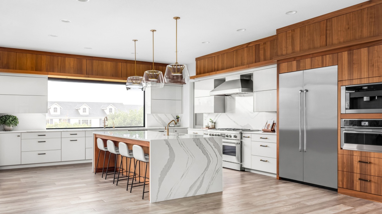 Beautiful kitchen in new luxury home with large waterfall island, stainless steel appliances, white cabinets, and hardwood floors