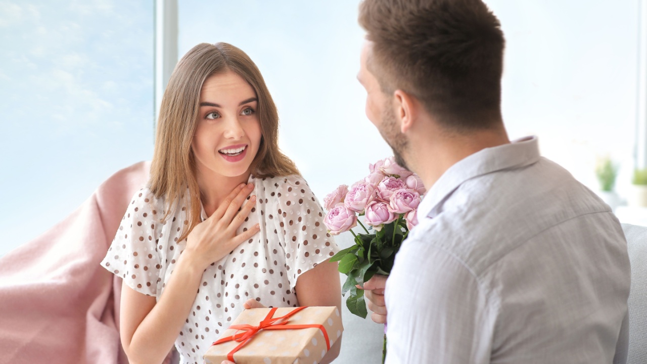 Man giving bouquet of flowers and gift to his girlfriend at home