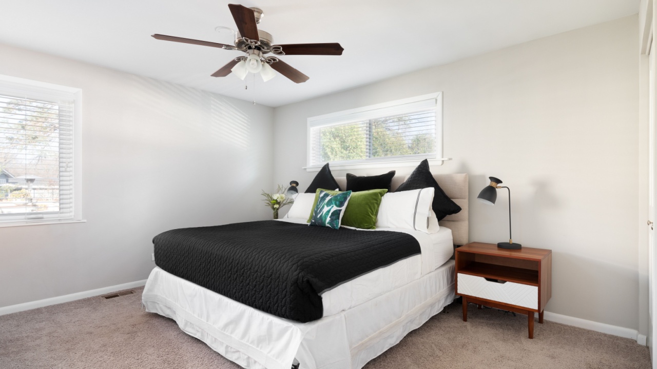 ELMHURST, IL, USA - NOVEMBER 13, 2020: A bedroom with a large bed with black, white, and green bedding and a wooden nightstand.