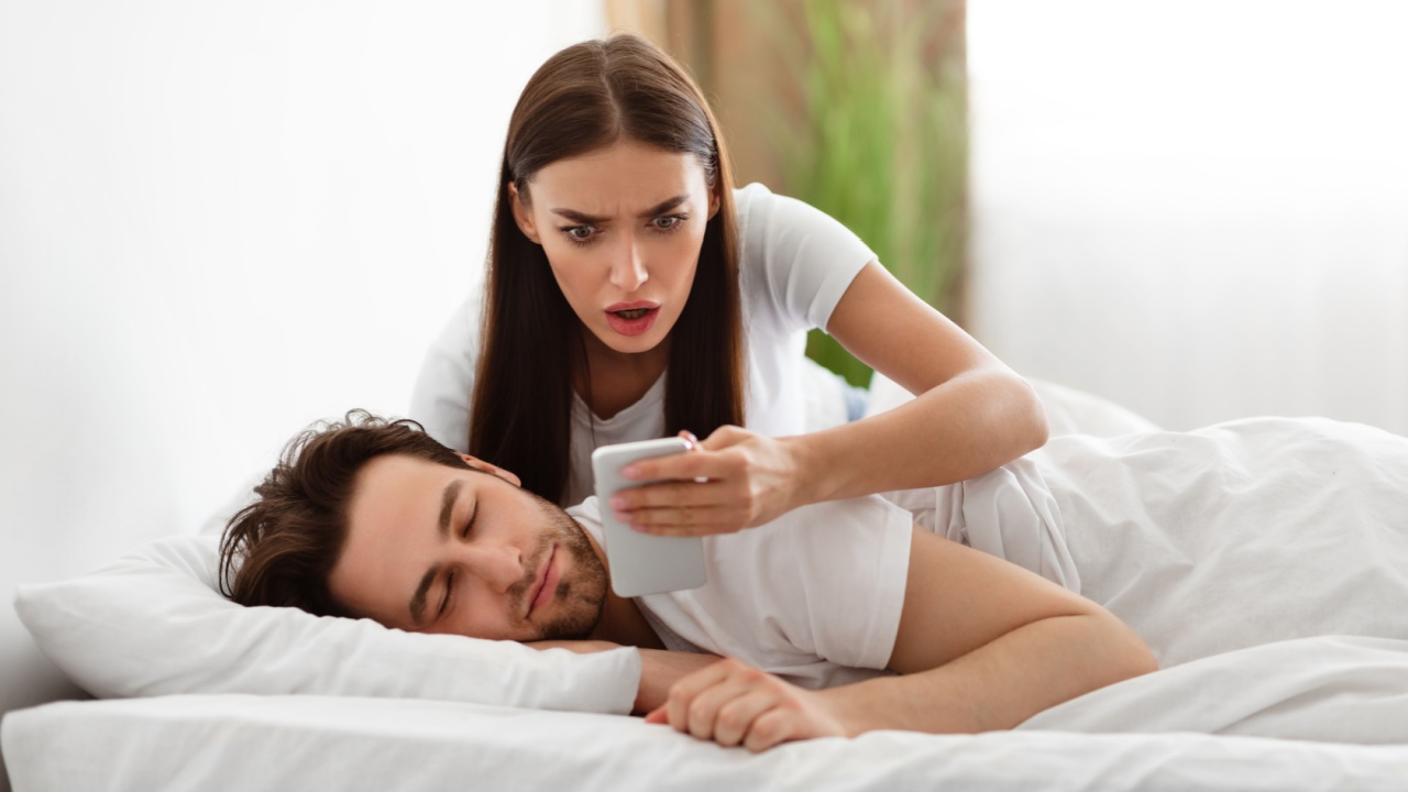 Infidelity. Shocked Wife Reading Message From Lover On Phone While Cheating Husband Sleeping In Bedroom At Home. Jealous Woman Checking Boyfriend's Cellphone Chats. Affair, Relationship Issues