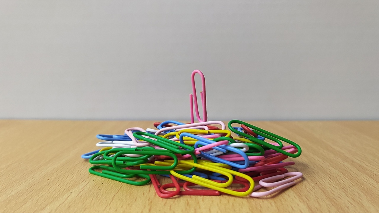 Unique one pink paper clip stand out and against other stack of colorful paperclips crowd on table.