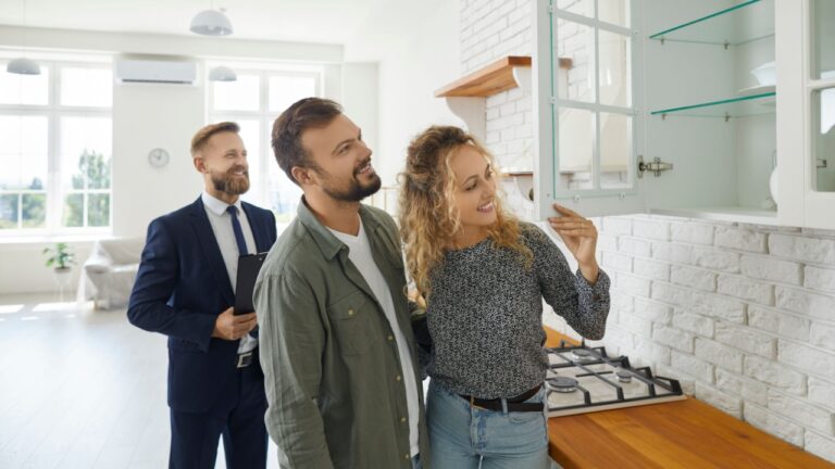 Boyfriend and girlfriend buying house. First time buyers or future tenants meeting real estate agent and looking around new home. Husband and wife looking at good quality modern wooden kitchen cabinet