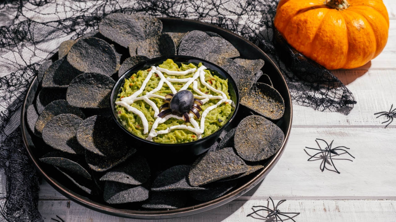 Spooky Halloween black potato chips with guacamole dip: appetizer into a Halloween with of black olive spider