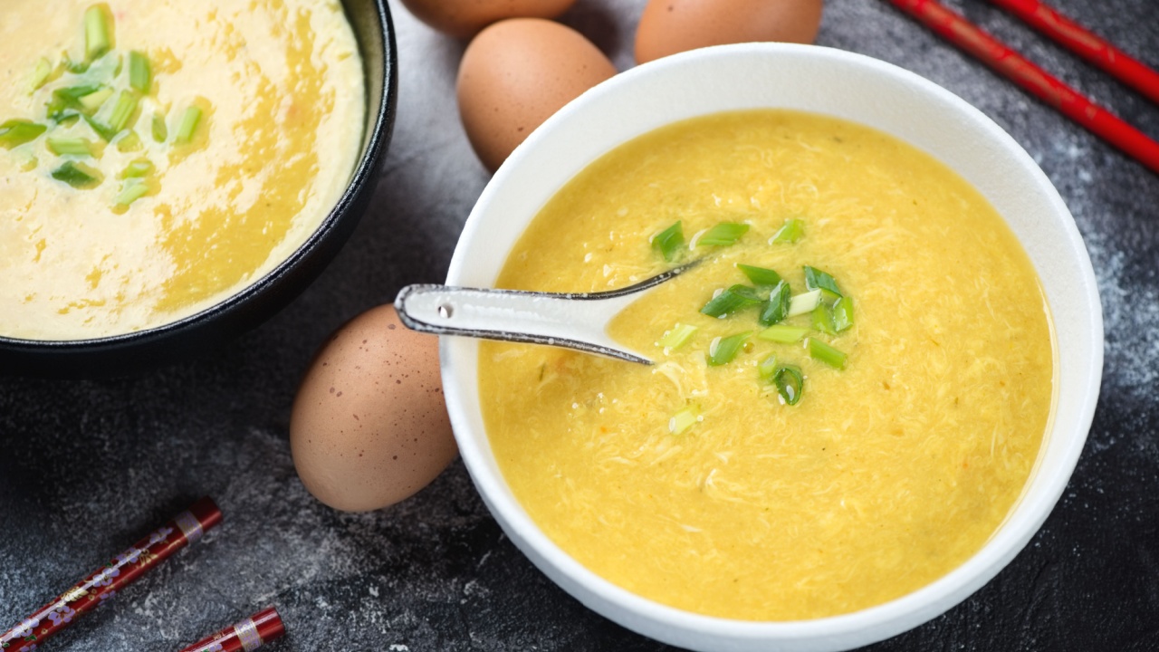 Black and white bowls of chinese egg-drop soup topped with chopped scallions, horizontal shot on a dark-grey stone background