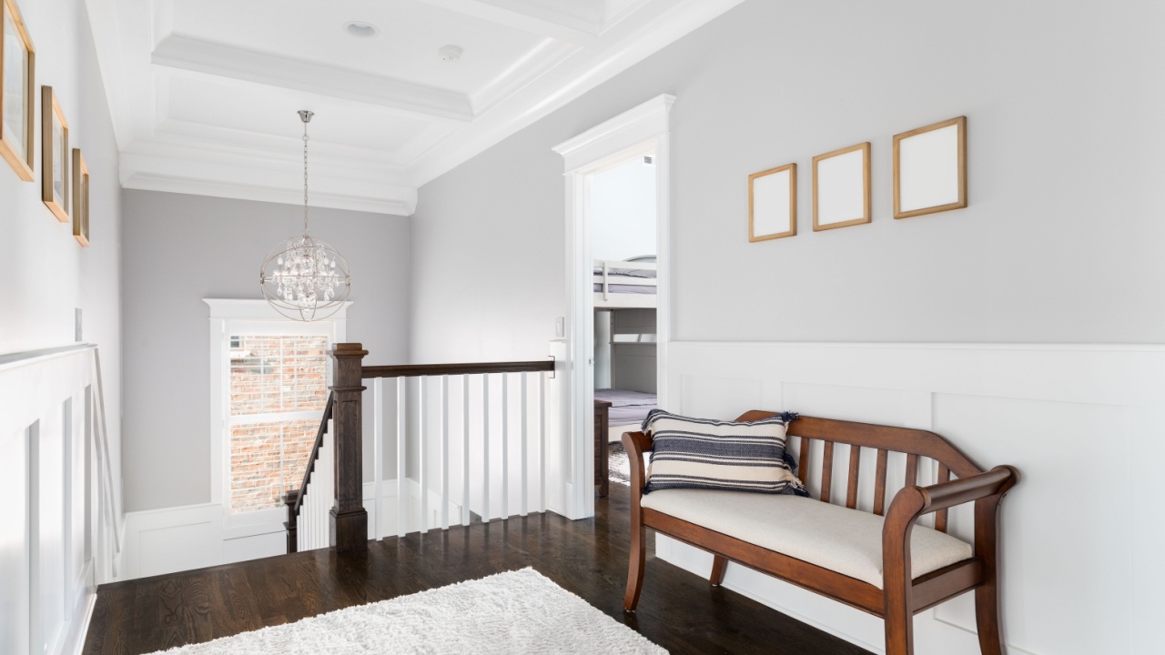 An upstairs hallway in a luxury home with a coffered ceiling, dark hardwood floor, a wooden bench, and board and batten walls.