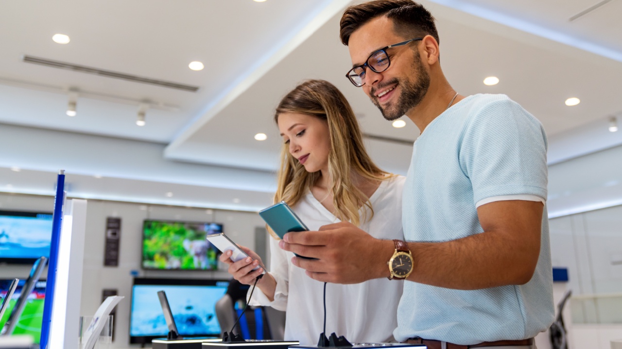 Tech shopping device gadget concept. Happy young people buying a new smartphone in mobile shop.