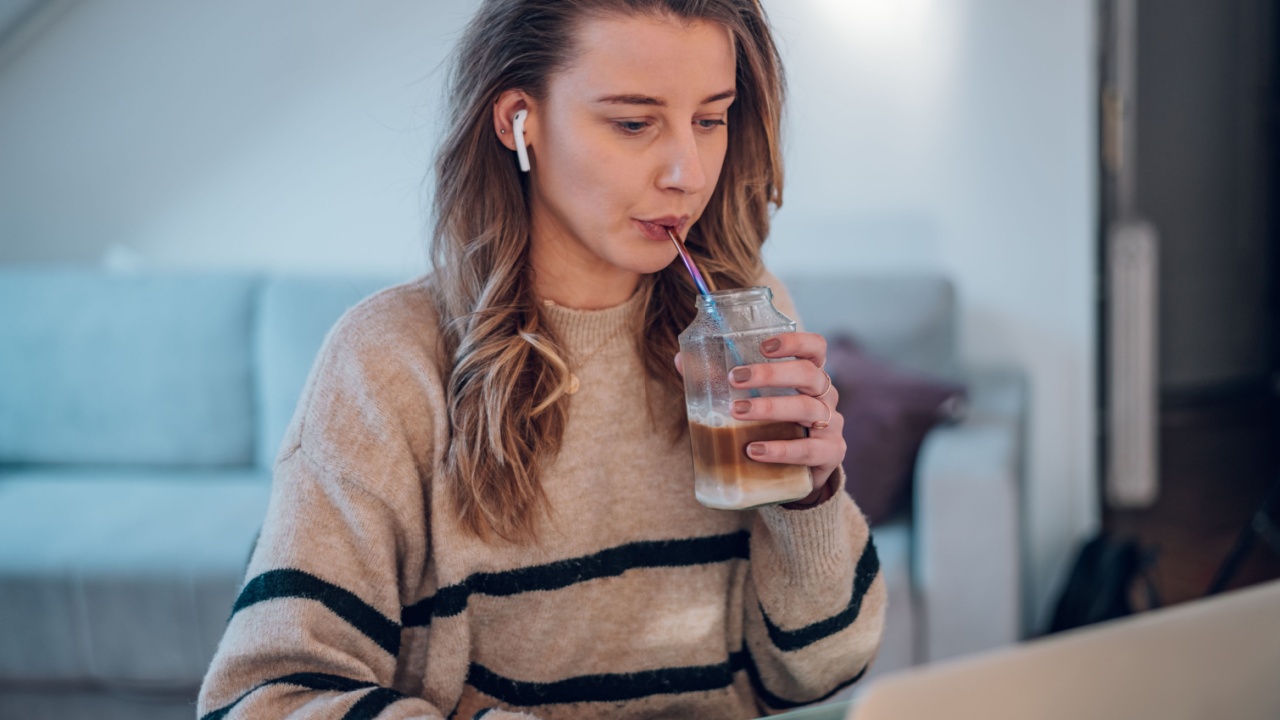 Young creative woman working from home while using a laptop and drinking coffee with a metal ecology straw. Reusable straw.