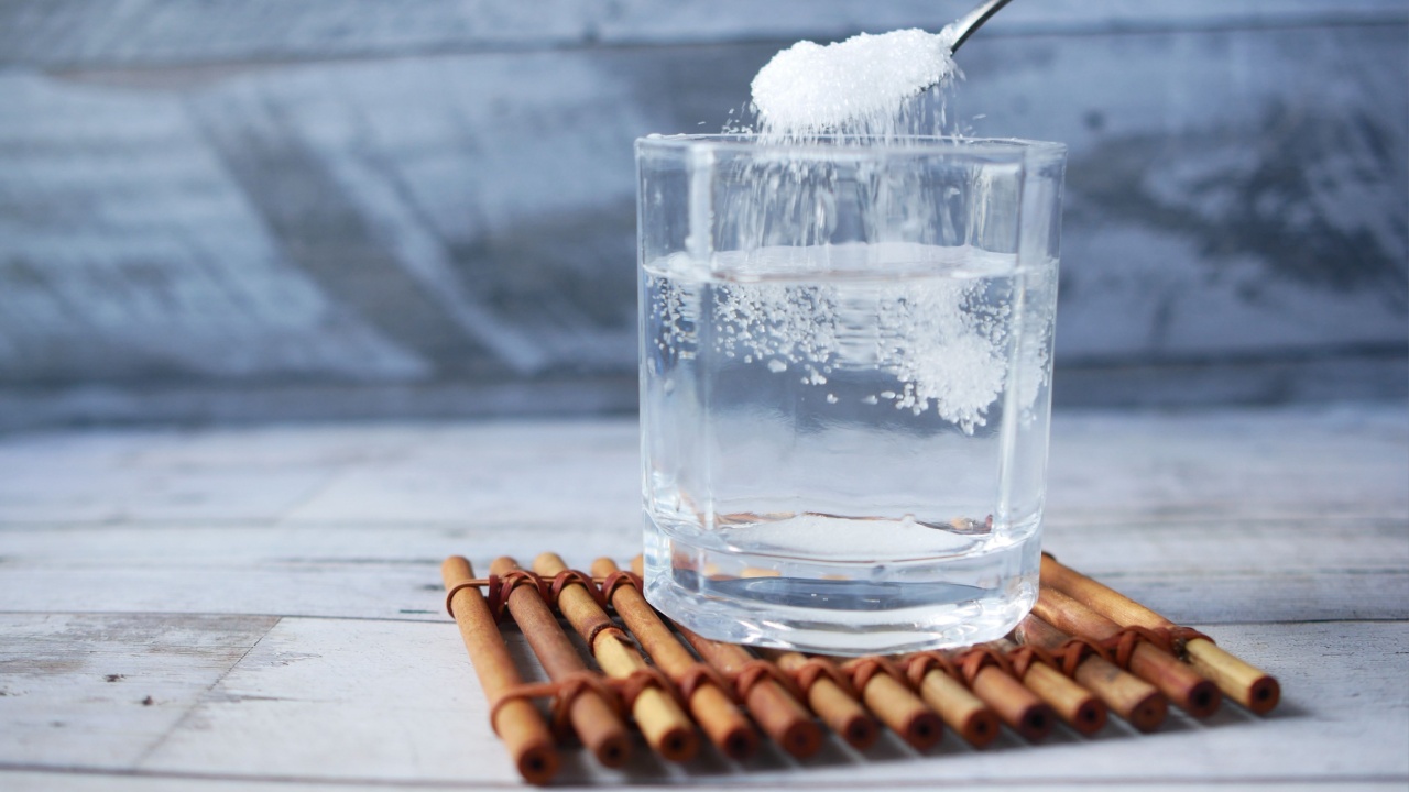 pouring white sugar in a glass of water on table