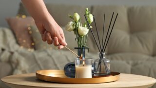 Woman lighting candle at wooden table in living room, closeup