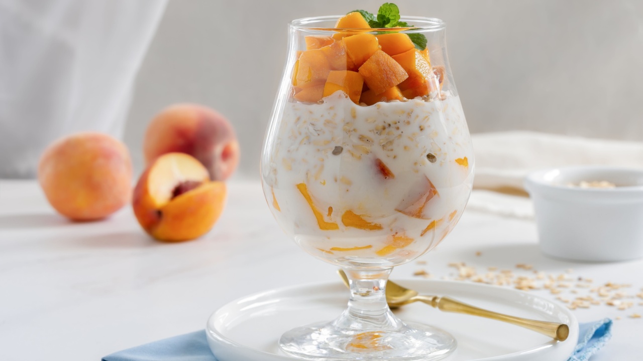 Peaches and Cream Overnight Oats. Healthy breakfast made with oats soaked for the night in milk or yogurt layered with cubes of fresh peaches, served in a clear glass.