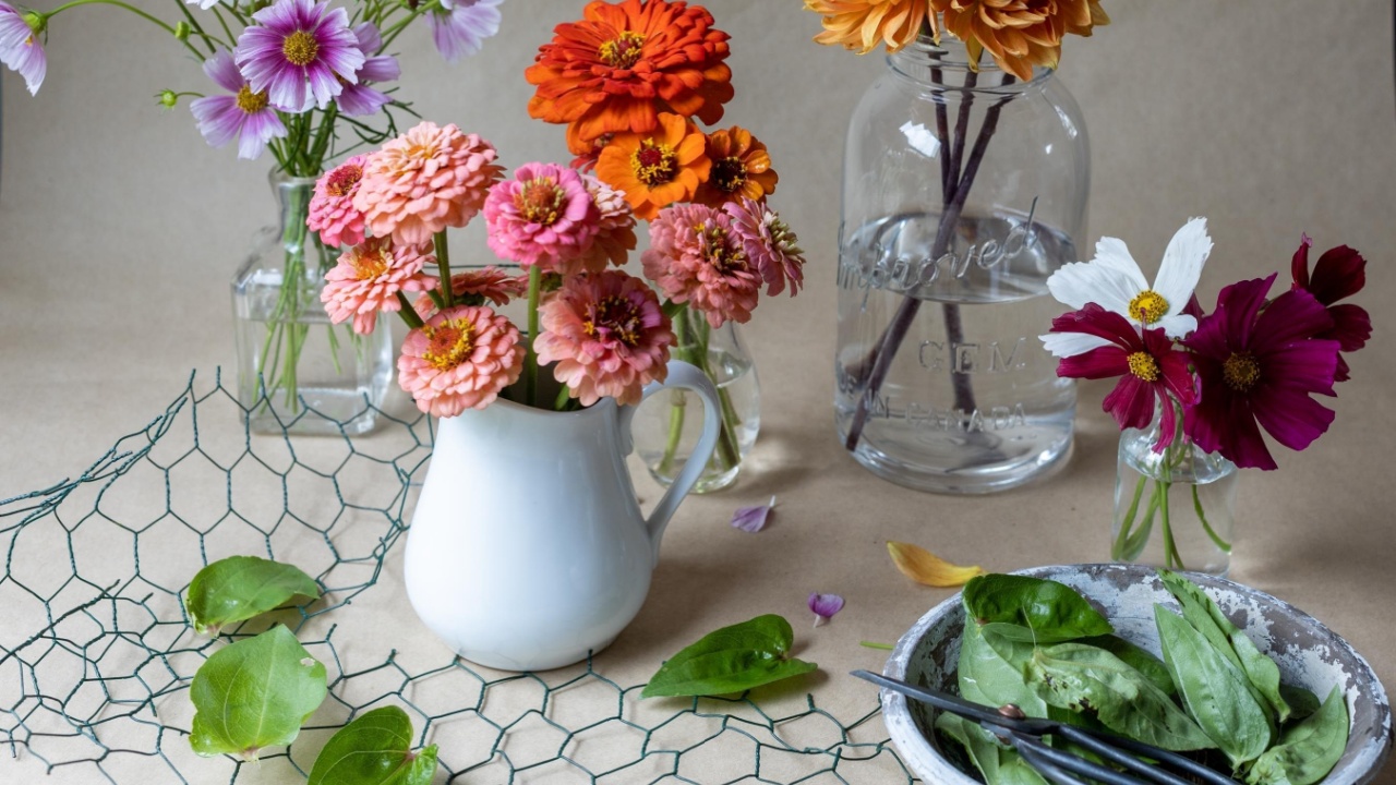 A casual setting of garden flowers arranged in assorted vases with chicken wire surface and kraft paper back ground