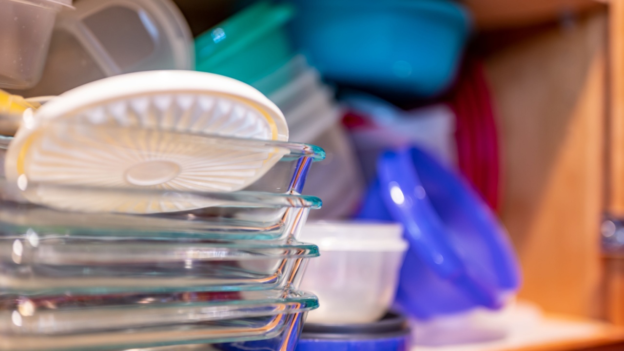 Narrow depth of field picture of an open kitchen cabinet with an assortment of containers and mismatched lids stacked.