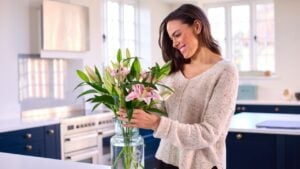 Smiling Woman At Home Arranging Bouquet Of Flowers In Glass Vase