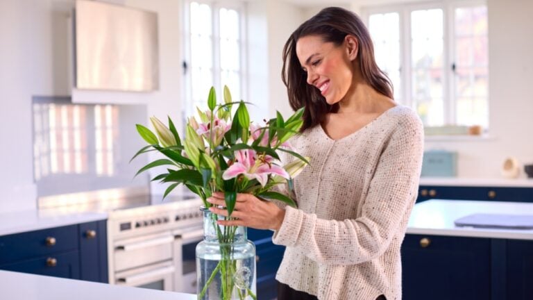 Smiling Woman At Home Arranging Bouquet Of Flowers In Glass Vase