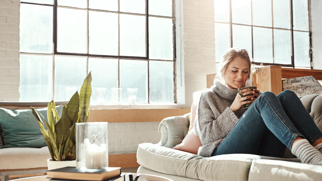 Woman relax in living room, coffee and peace on sofa, content at home with lifestyle and happiness. Female in apartment, happy woman and coffee cup, positive energy and mindset with wellness